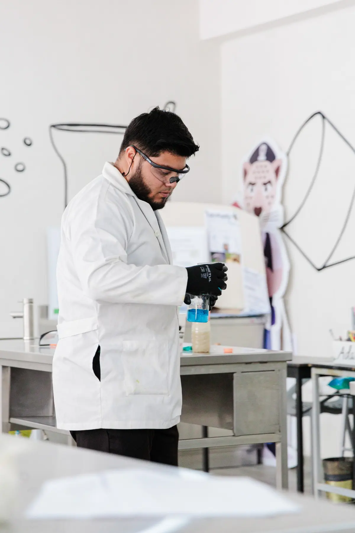 Maestro con bata y lentes de seguridad haciendo un experimento en el laboratorio