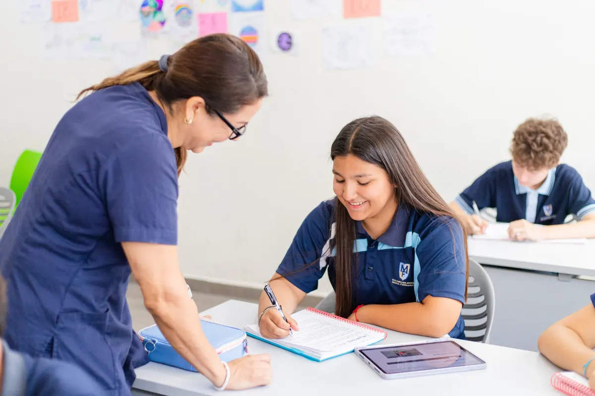Maestra revisando el trabajo de una alumna de secundaria que sonríe