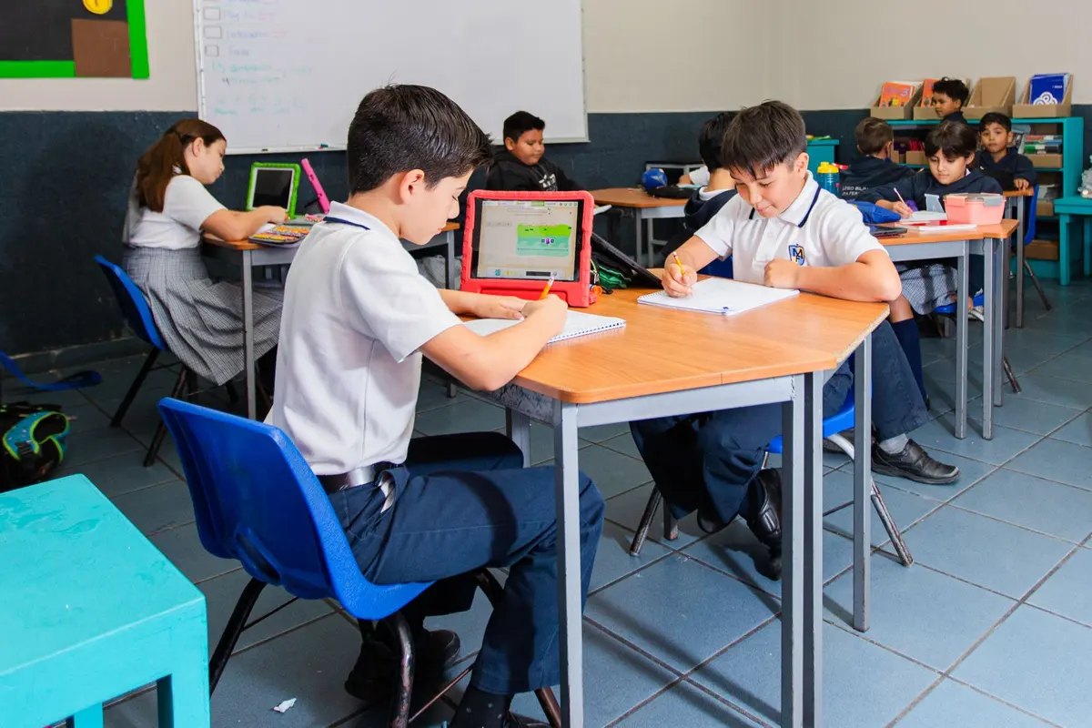 Alumnos de primaria trabajando en su salón con cuaderno e iPad