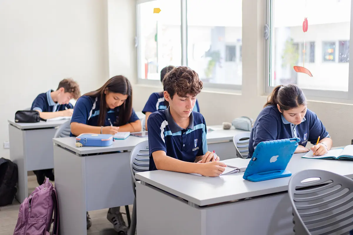 Alumnos de secundaria trabajando en su salón con cuaderno e iPad